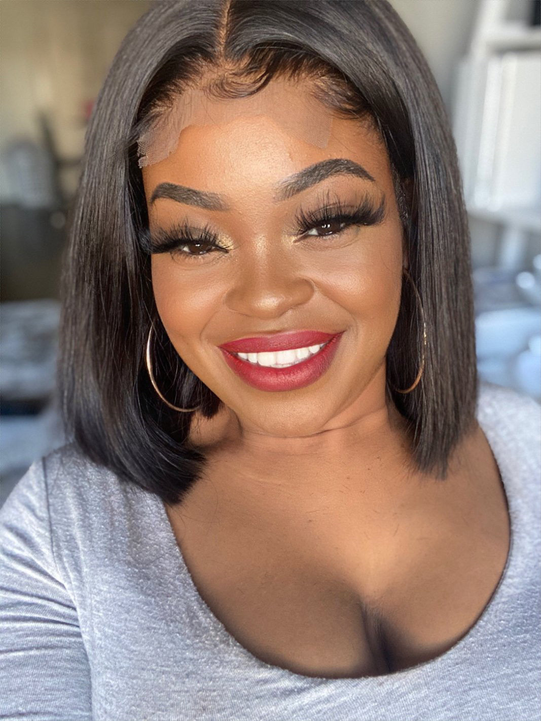 A woman wearing a glossy, lace front wig with a smile on her face. The wig has a natural hair color and style, giving a realistic look.