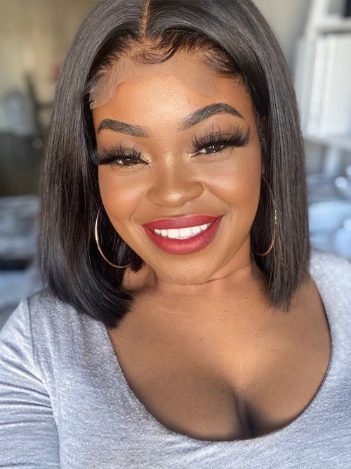 A woman wearing a glossy, lace front wig with a smile on her face. The wig has a natural hair color and style, giving a realistic look.